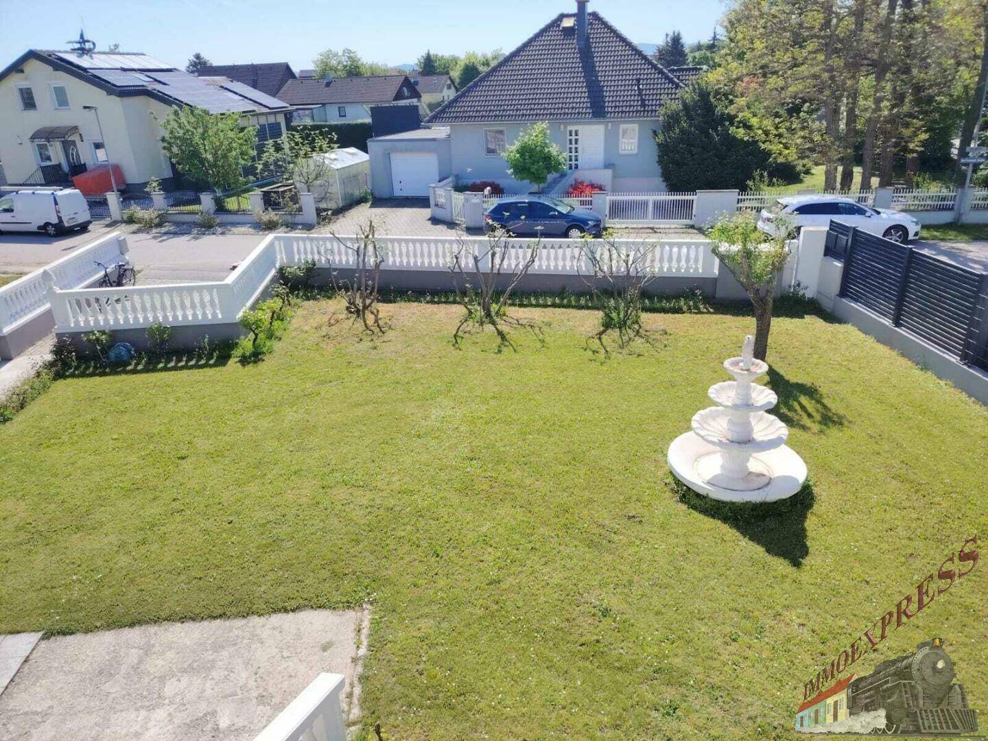 Weitläufiger Garten mit Rasenfläche und dekorativem Brunnen, umgeben von einer niedrigen Mauer.