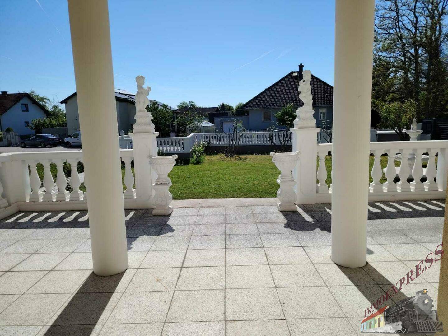 Überdachter Eingangsbereich mit Säulen und Fliesenboden, der zum Garten und zur Straße führt.