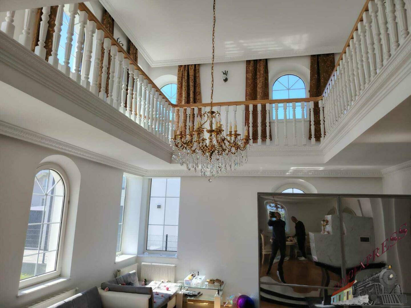 Großzügiges Wohnzimmer mit hoher Decke, Galerie und elegantem Kronleuchter, lichtdurchflutet.
