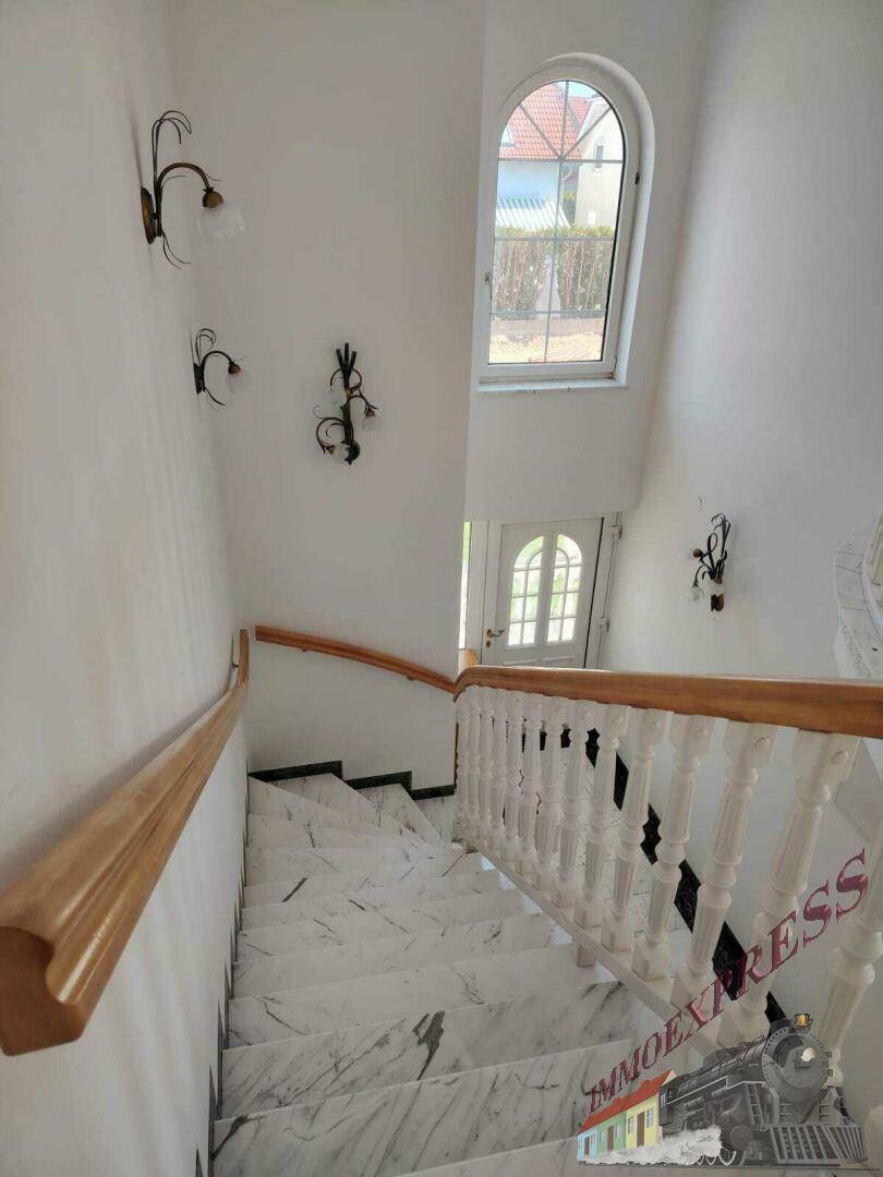 Elegante Marmortreppe mit Holzgeländer und Bogenfenster, die den Eingangsbereich erhellt.