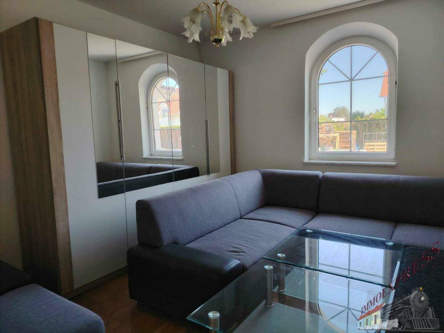 Gemütliches Wohnzimmer mit Sofa, Spiegelschrank und großen Rundbogenfenstern für viel Licht.