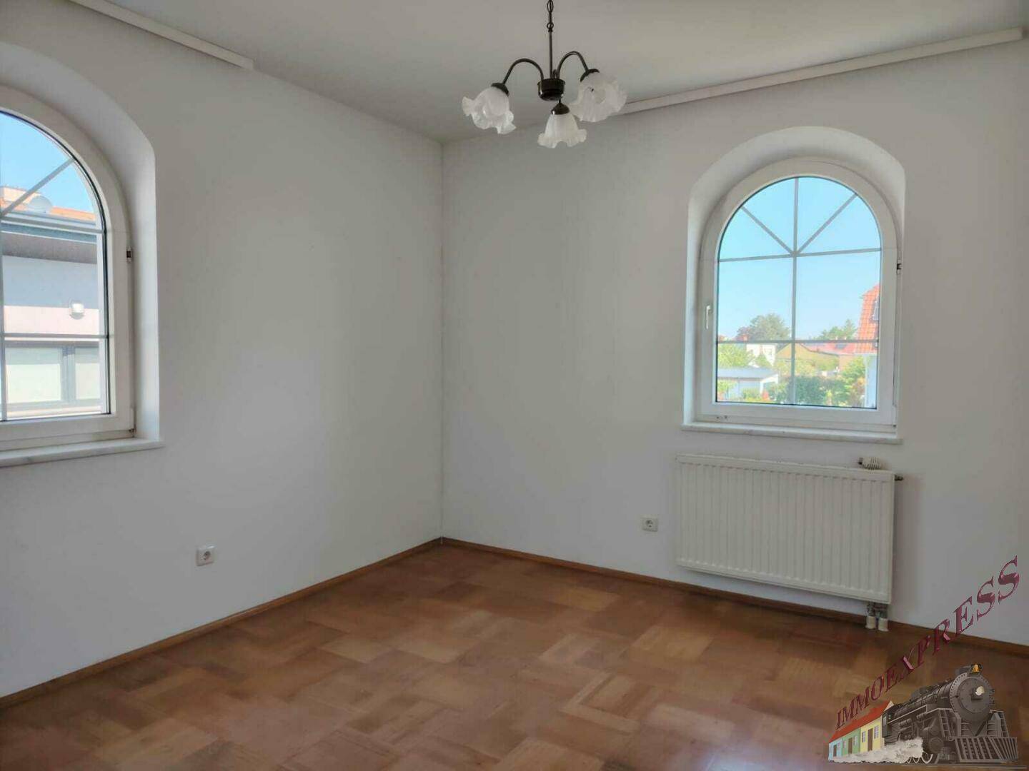Helles Zimmer mit Parkettboden und zwei Rundbogenfenstern, ideal als Schlaf- oder Arbeitszimmer.