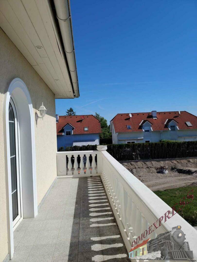 Geräumiger Balkon mit Balustrade und Blick auf die Umgebung unter blauem Himmel.