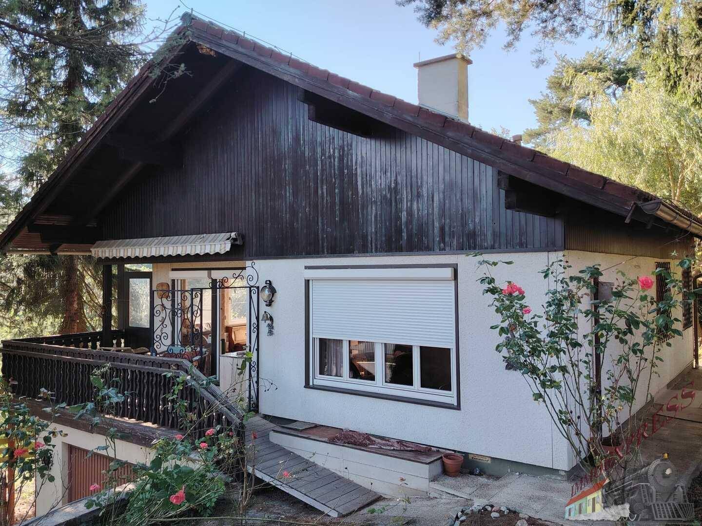 Seitenansicht des Hauses mit Holzbalkon, Rollladenfenster und umgebender Natur.