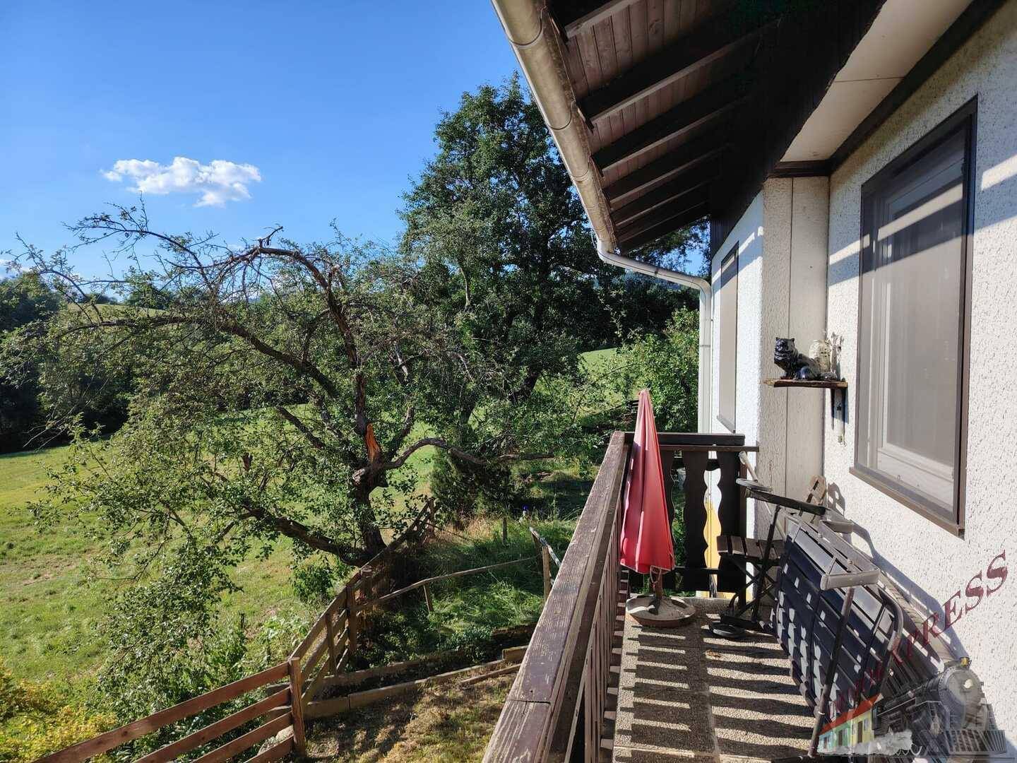 Balkon mit Holzboden und Geländer, bietet einen weiten Blick auf die grüne Landschaft.