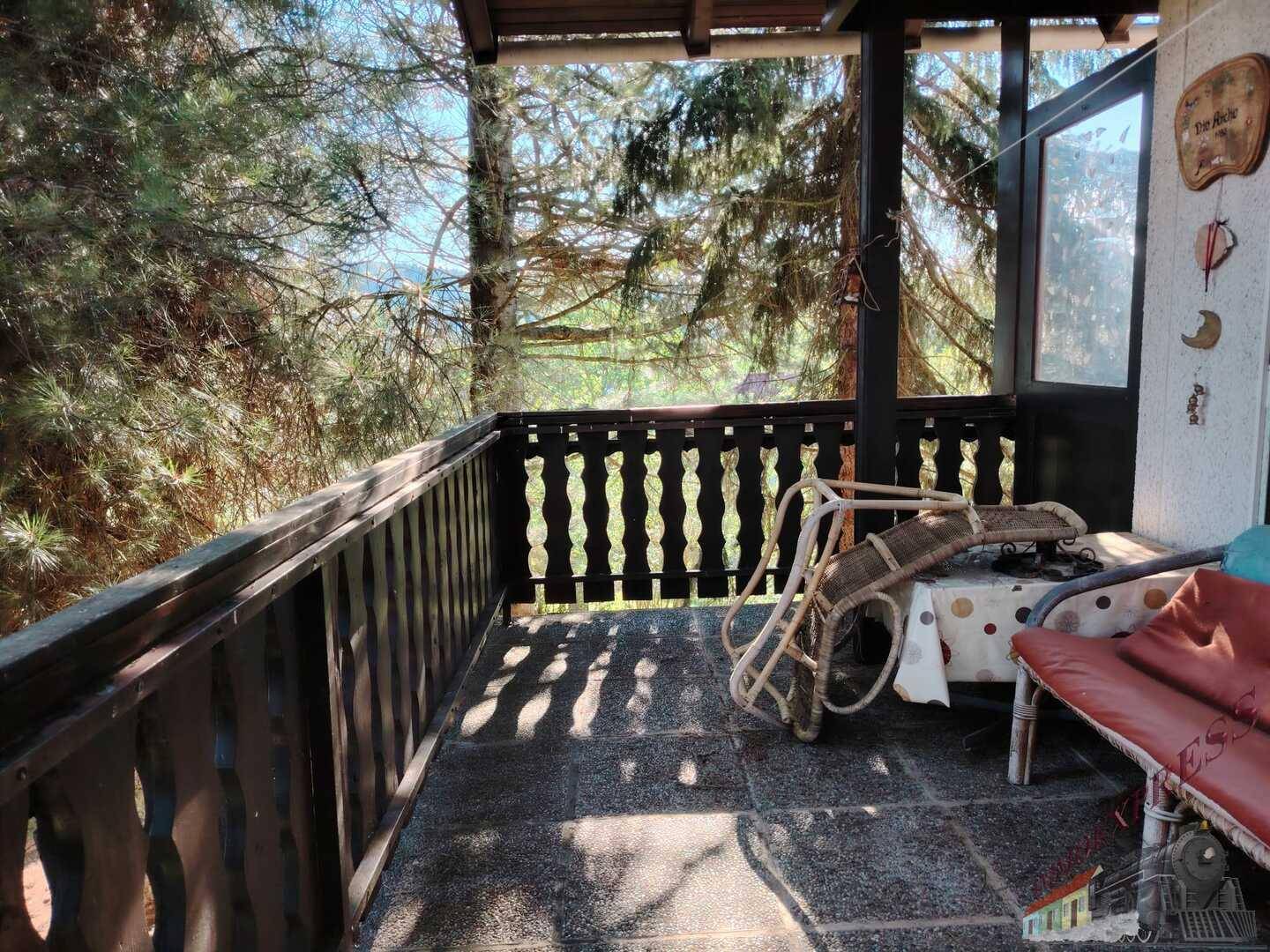 Überdachter Balkon mit rustikalem Holzgeländer und Blick auf hohe Bäume.