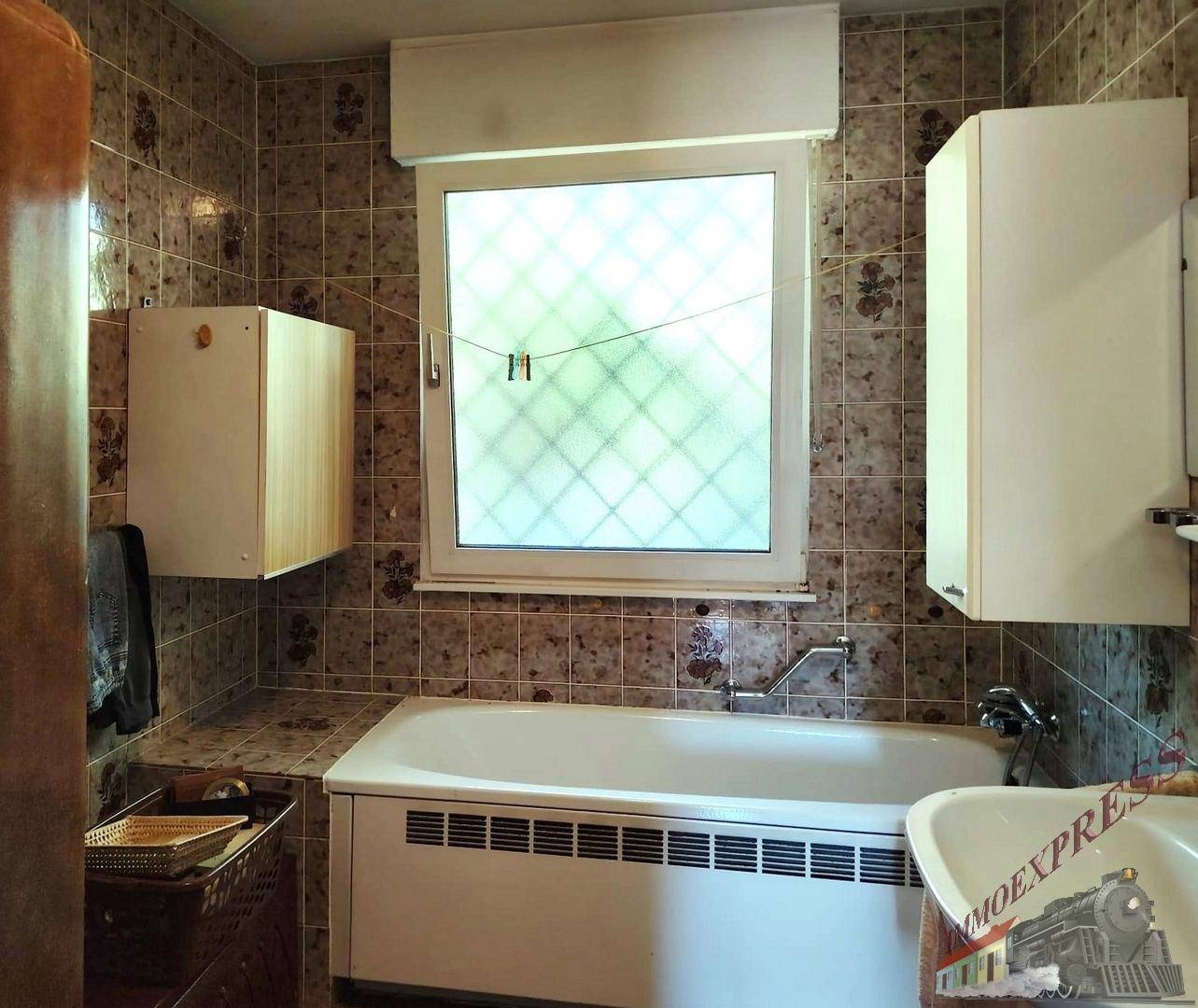 Badezimmer mit Badewanne, gefliesten Wänden und einem Fenster für Tageslicht.