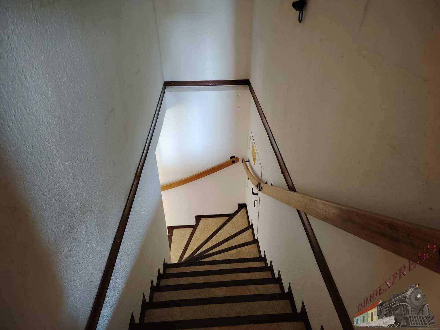 Treppenhaus mit Holzgeländer und Stufen, die in ein weiteres Stockwerk führen.