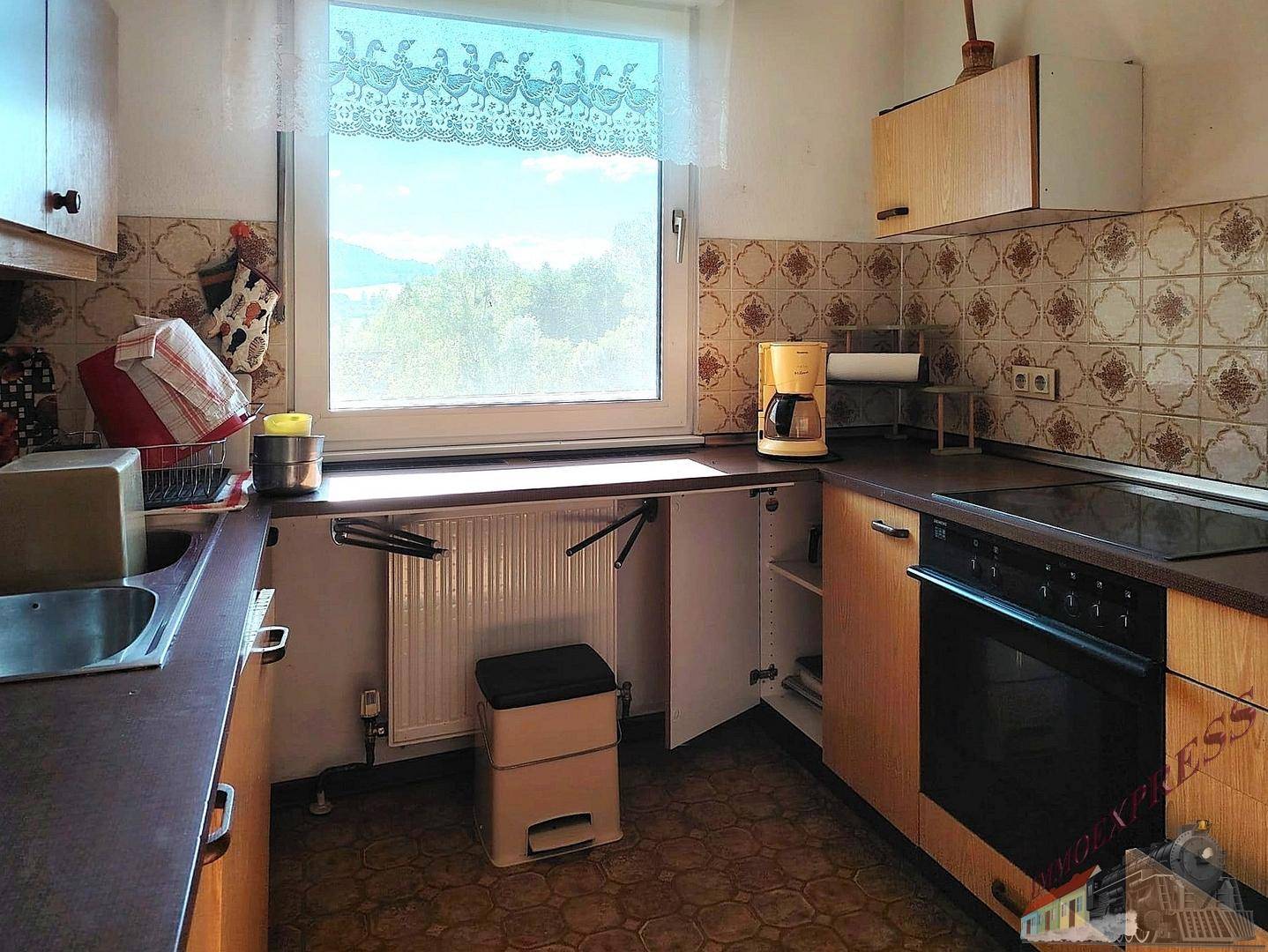 Funktionale Küche mit Holzschränken, Fliesenboden und Fenster mit weitem Ausblick.