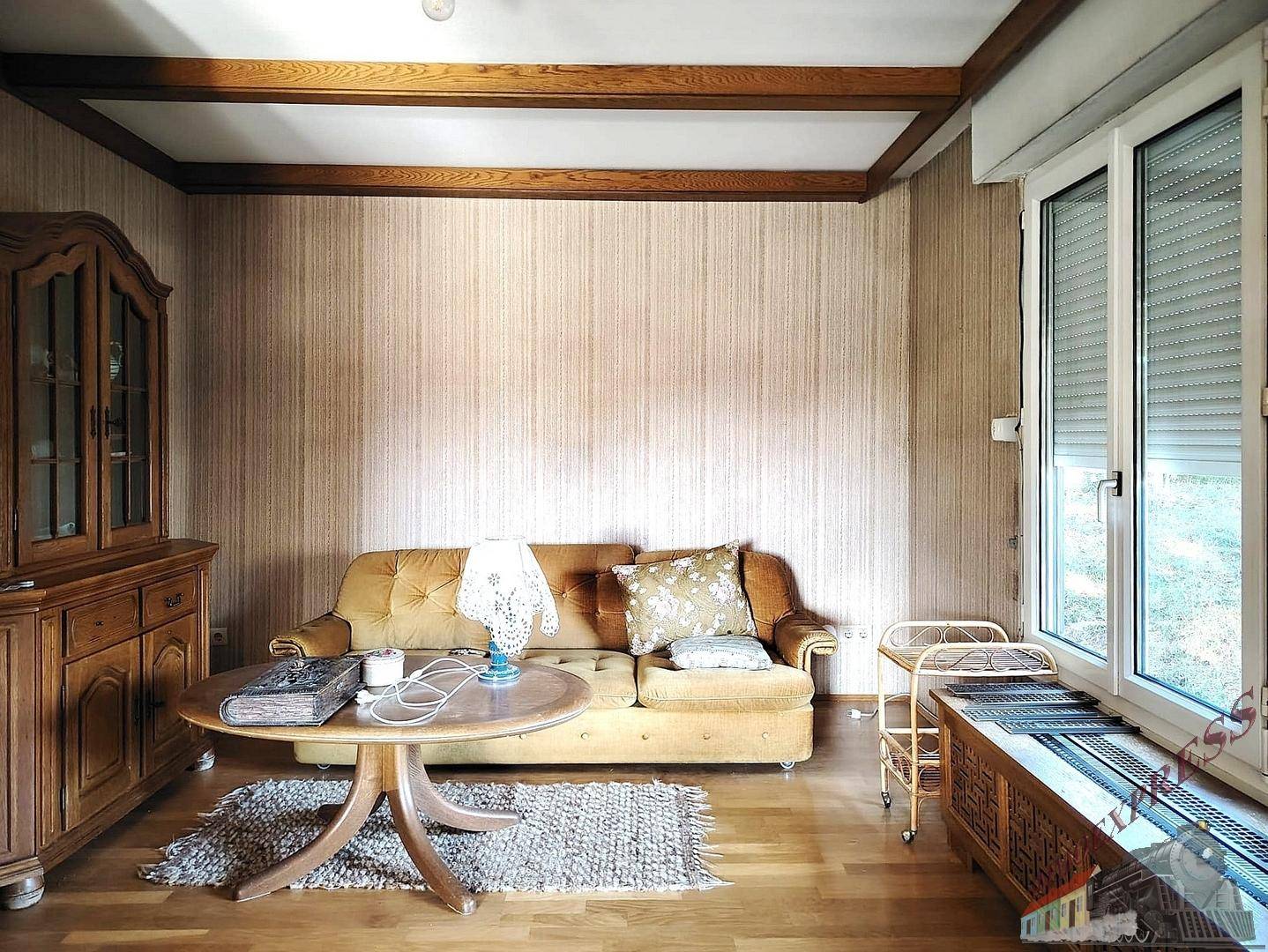 Wohnzimmer mit bequemer Couch, Holzboden und Fenster mit Rollladen.