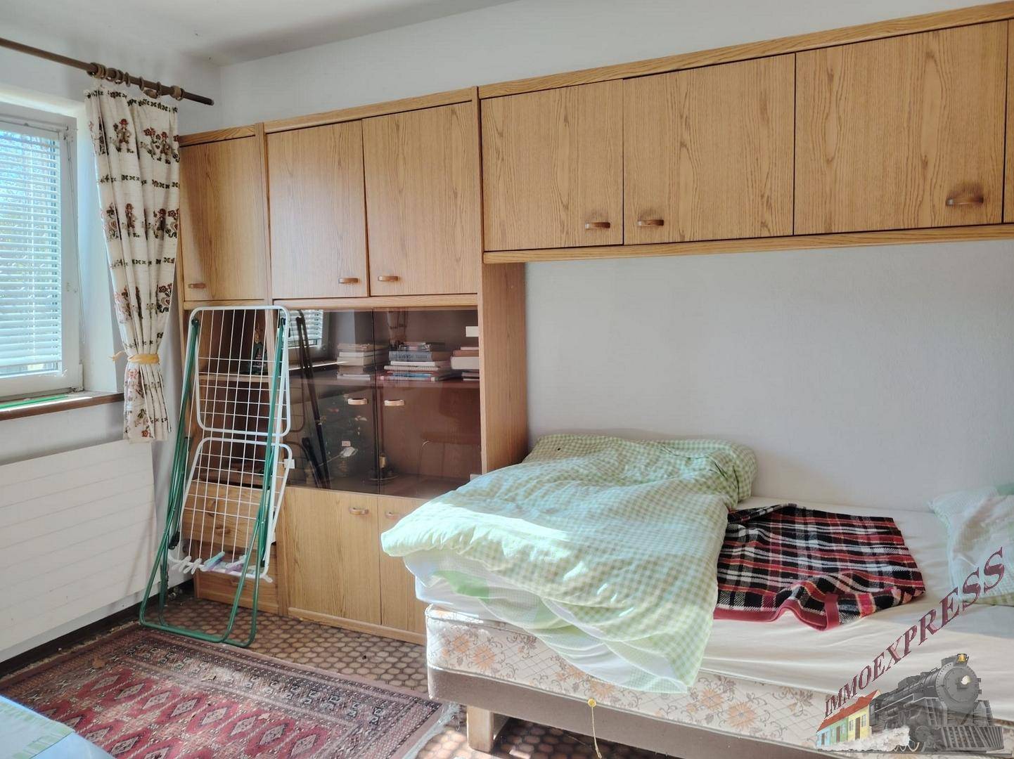 Schlafzimmer mit Bett, Einbauschränken und Fenster mit Jalousien.