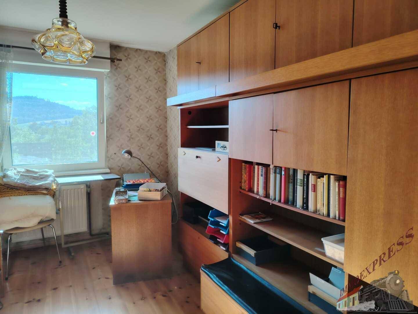 Arbeitszimmer mit Einbauschränken, Schreibtisch und Fenster mit Blick ins Grüne.