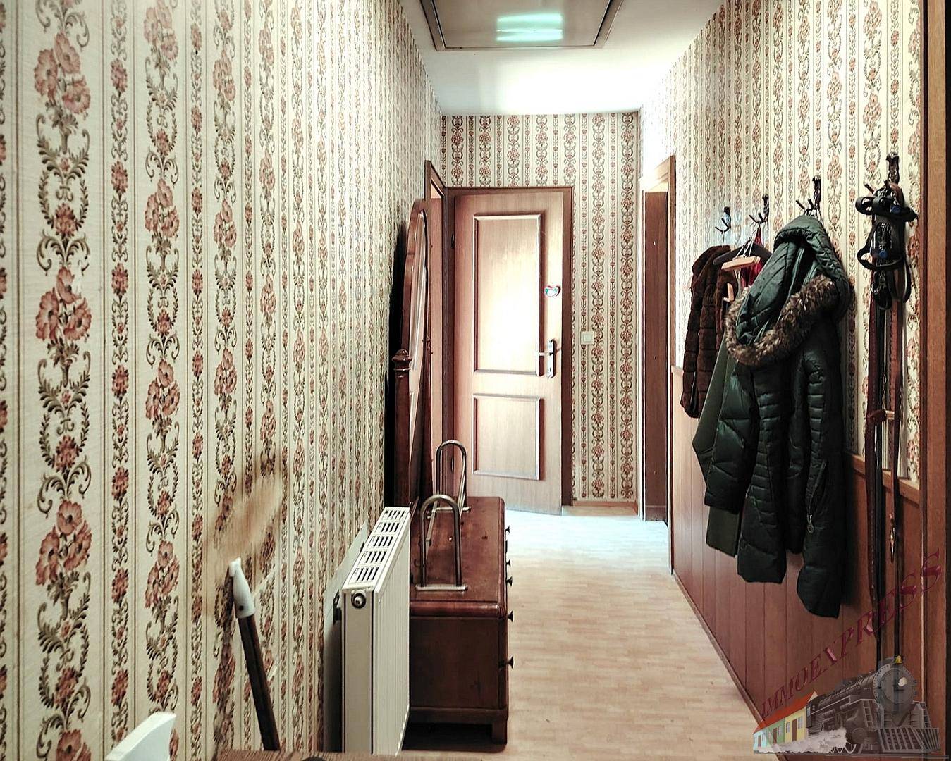 Flur mit floraler Tapete, Holzboden und Garderobe.