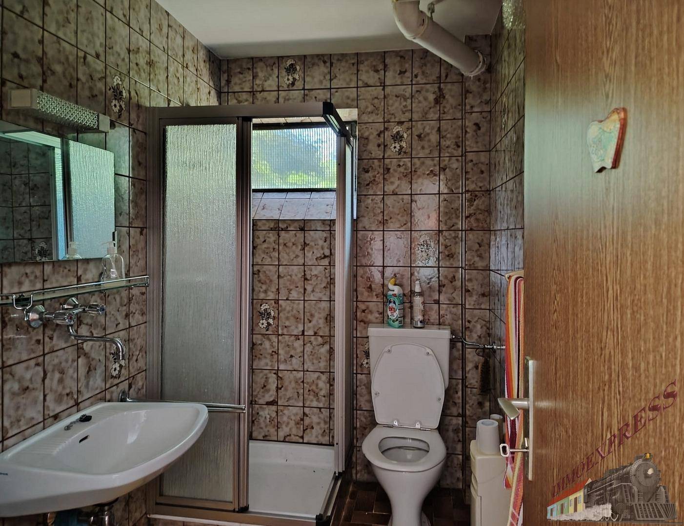 Badezimmer mit Dusche, WC und Waschbecken, komplett gefliest.