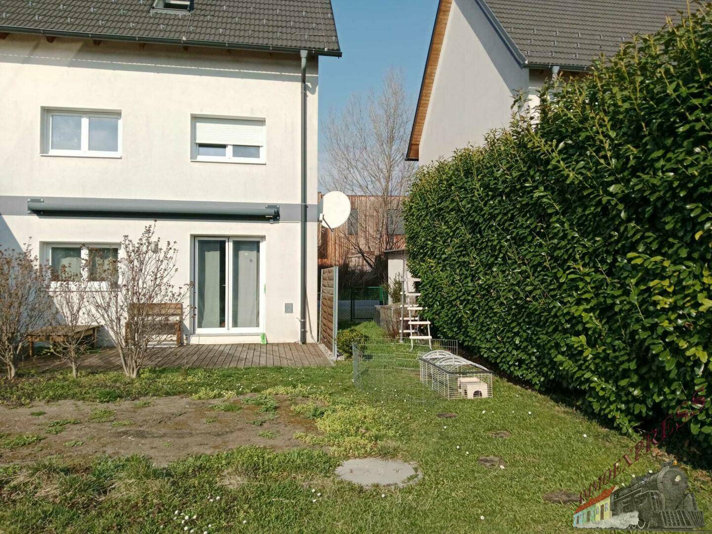 Hinterer Gartenbereich mit Holzterrasse, Rasen und hoher Hecke für Privatsphäre.