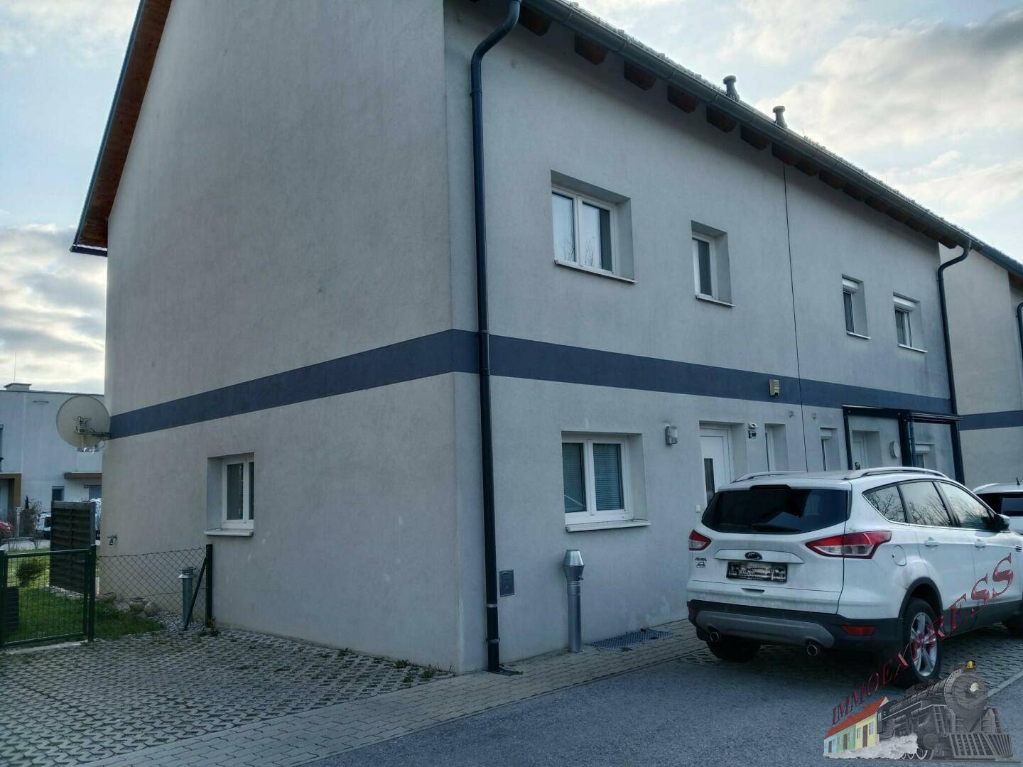 Seitenansicht des Reihenhauses mit Parkplatz und schlichter Fassadengestaltung.