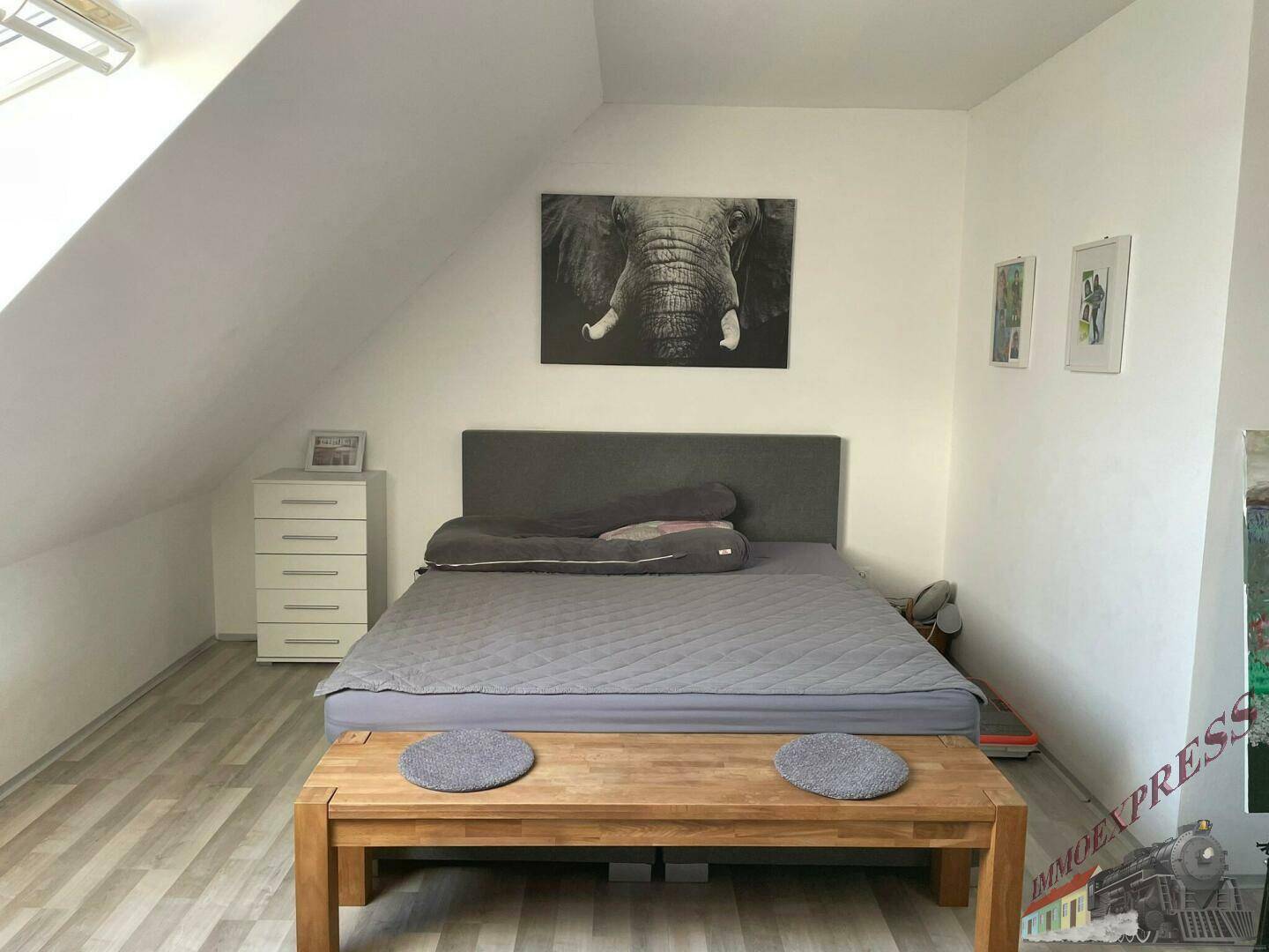 Schlafzimmer im Dachgeschoss mit schräger Decke, Doppelbett und Kommode.