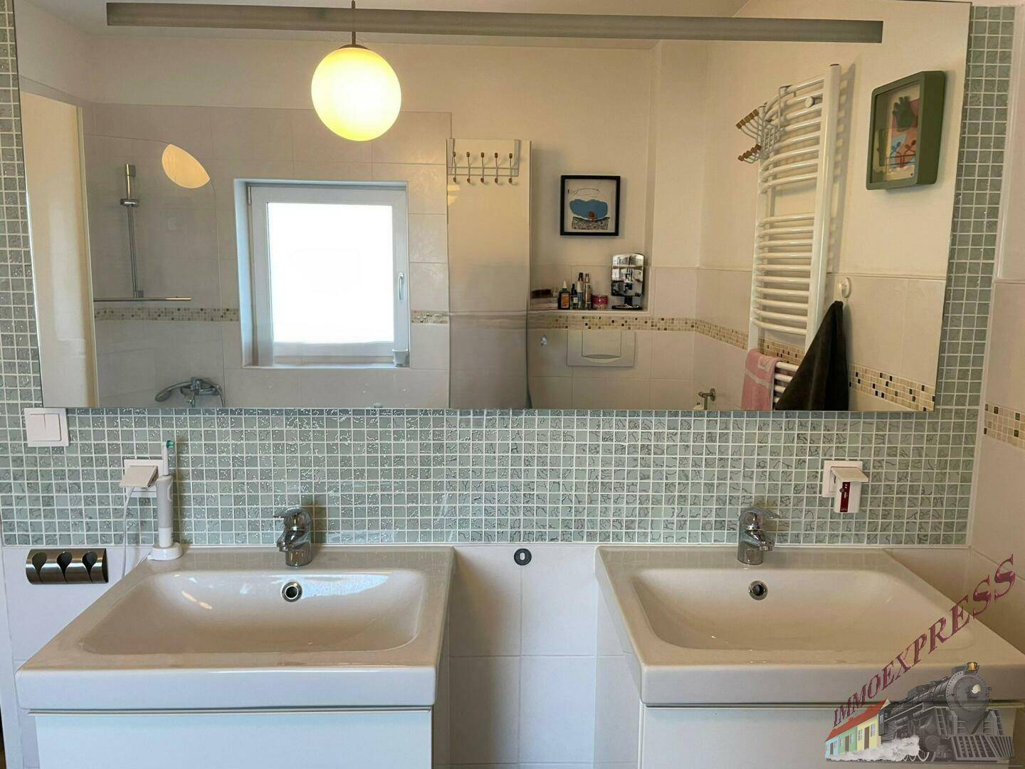 Badezimmer mit großem Spiegel, Doppelwaschbecken und Mosaikfliesen über dem Waschtisch.
