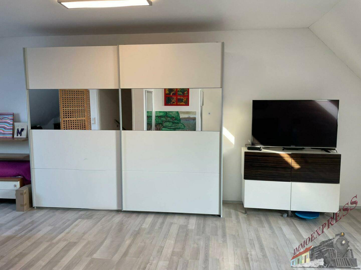 Dachgeschosszimmer mit großem Spiegelschrank und Fernseher, funktional eingerichtet.