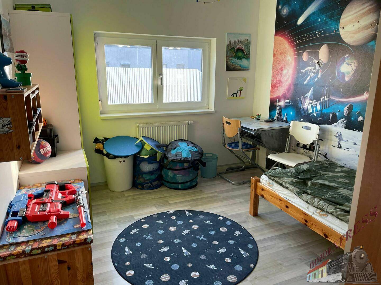 Kinderzimmer mit Bett, Schreibtisch, Spielzeug und Weltraum-Wanddekoration.