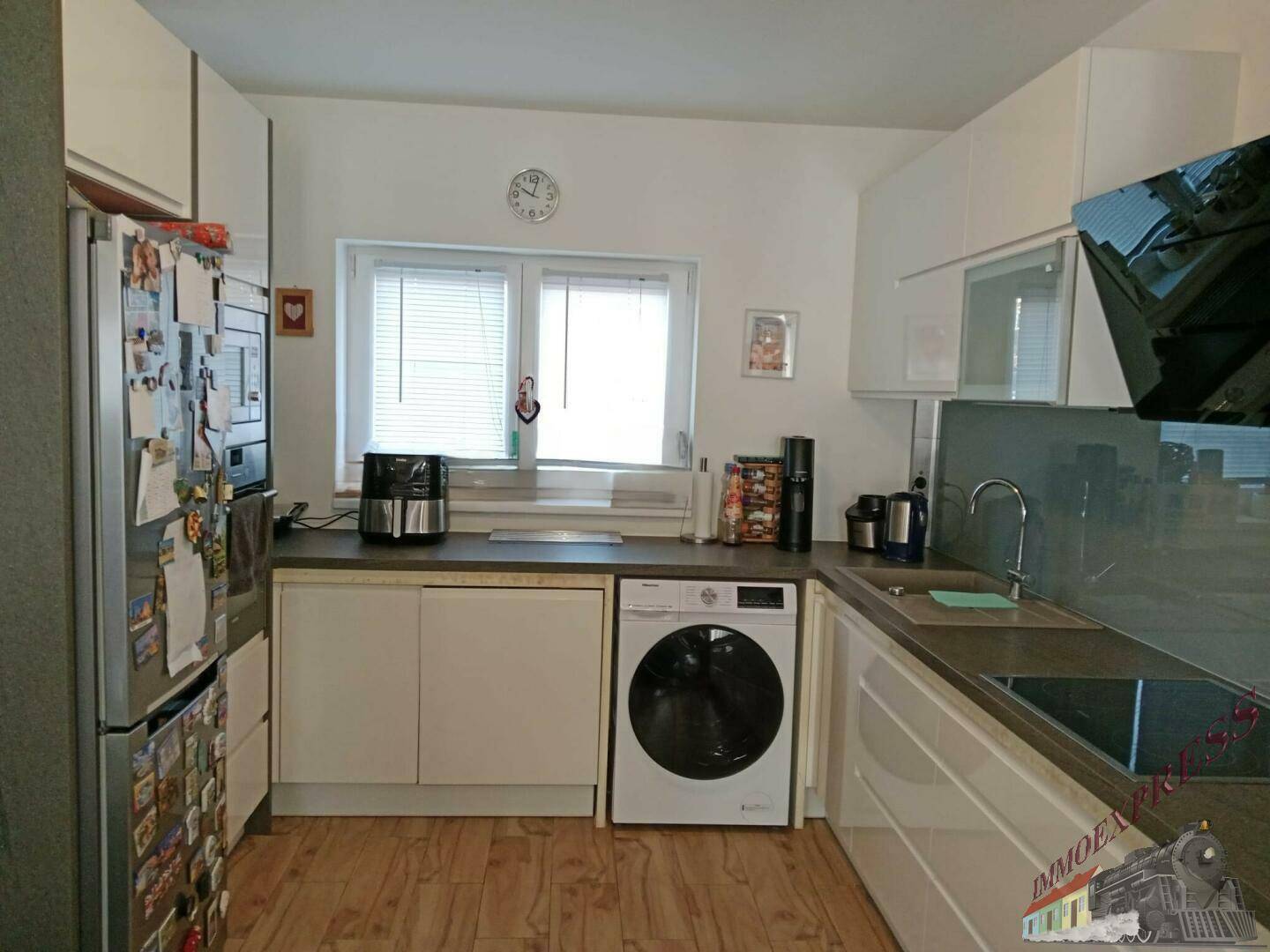 Funktionale Küche mit weißen Schränken, Fenster und integrierter Waschmaschine.