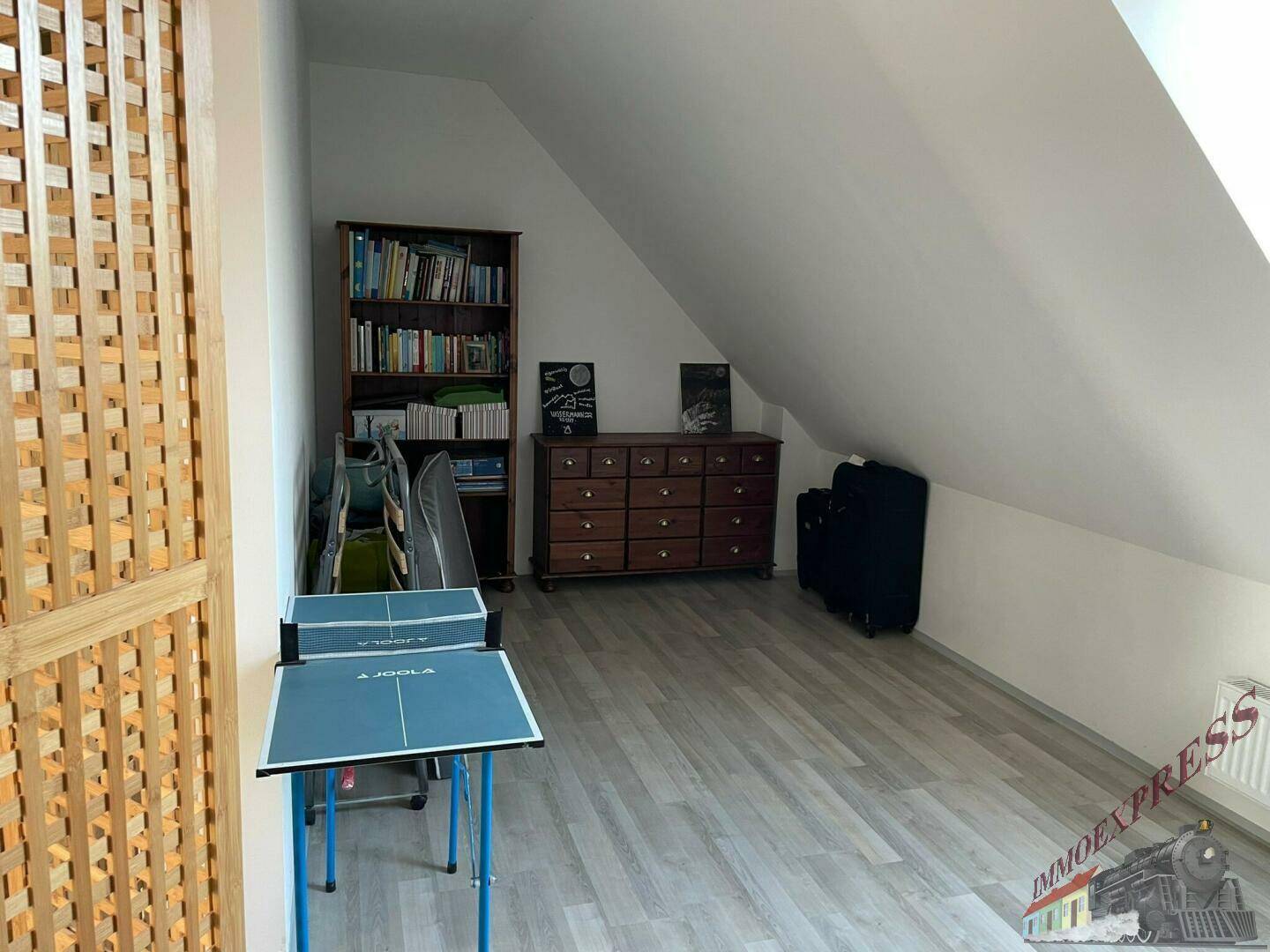 Geräumiges Dachgeschosszimmer mit Bücherregal und Tischtennisplatte, vielseitig nutzbar.
