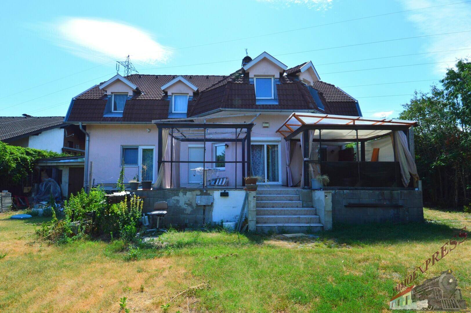 Rückseite des Hauses mit überdachter Terrasse und Treppe, die zum grünen Garten führt.