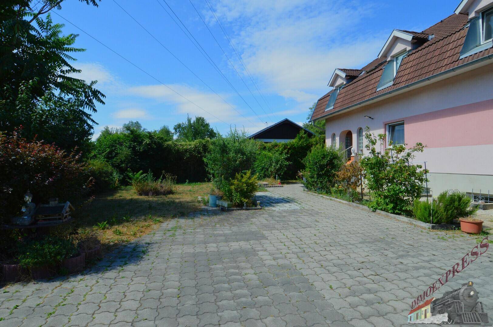 Gepflasterte Einfahrt und Vorgarten mit grünen Büschen und Rasenfläche vor dem Haus.
