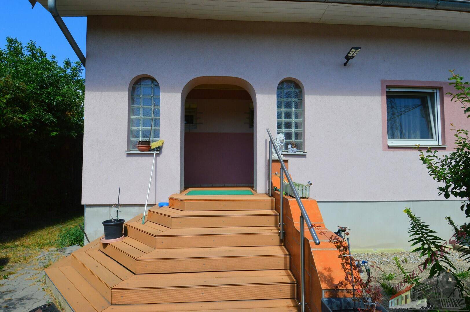 Hauseingang mit Holztreppe, Handlauf und dekorativen Glasbausteinfenstern.