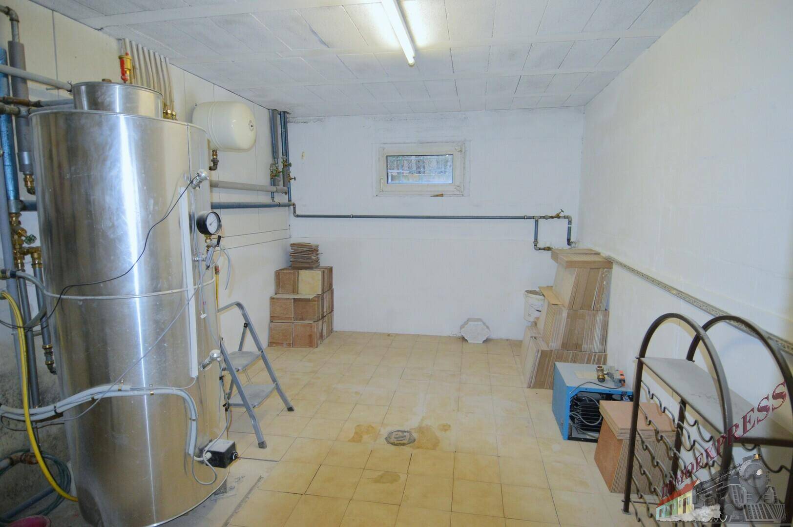 Hauswirtschaftsraum mit großem Warmwasserspeicher, Rohrleitungen und einem kleinen Fenster.