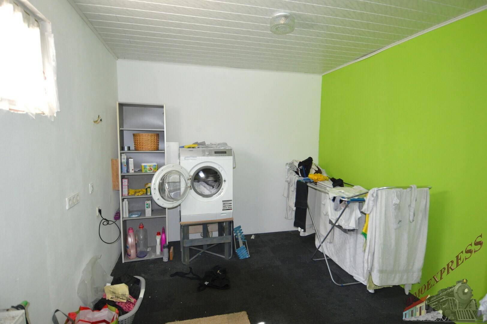 Praktischer Hauswirtschaftsraum mit Waschmaschine, Regalen und einer grünen Akzentwand zum Wäschetrocknen.