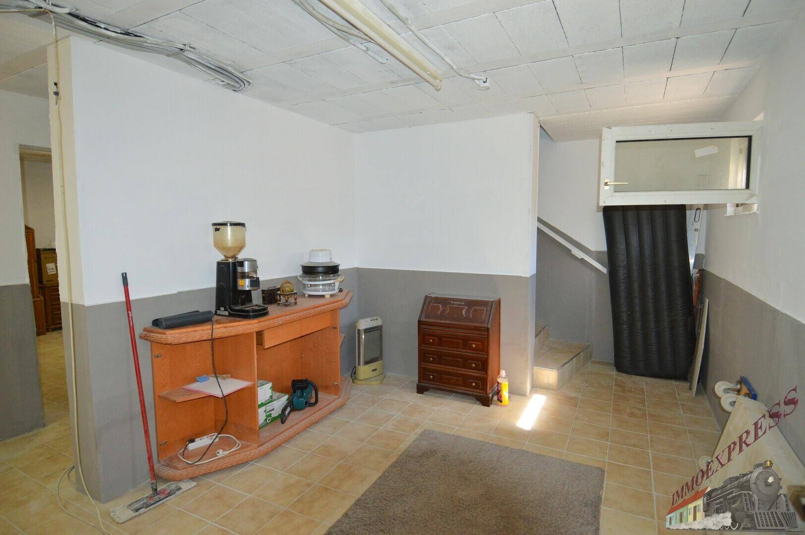 Kellerraum mit Fliesenboden, einem kleinen Fenster und einer Treppe, genutzt als Abstellfläche.