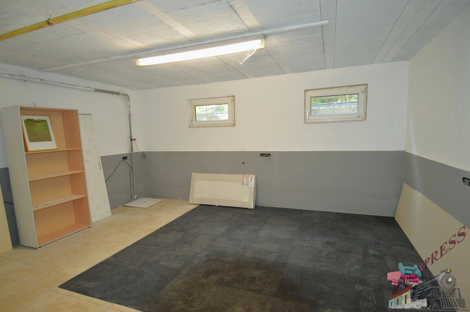 Unfertiger Kellerraum mit zwei kleinen Fenstern und Heizkörper, bereit für zukünftige Nutzung.