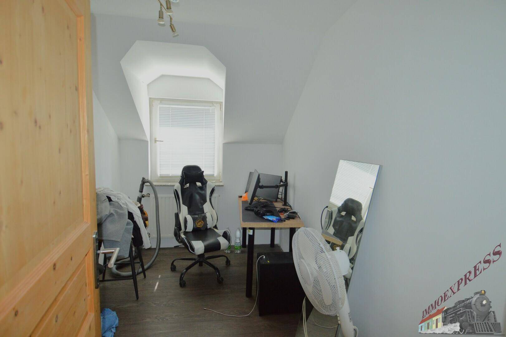 Dachgeschosszimmer als Büro genutzt mit Schreibtisch, Stuhl und Fenster.