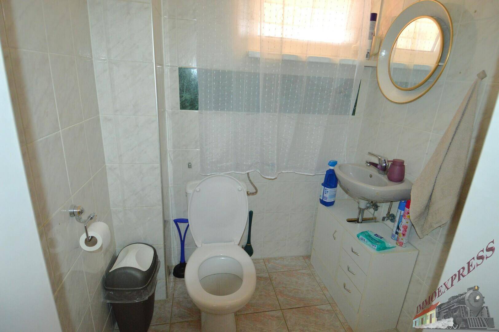 Separate Toilette mit Waschbecken, Spiegel und Fenster.