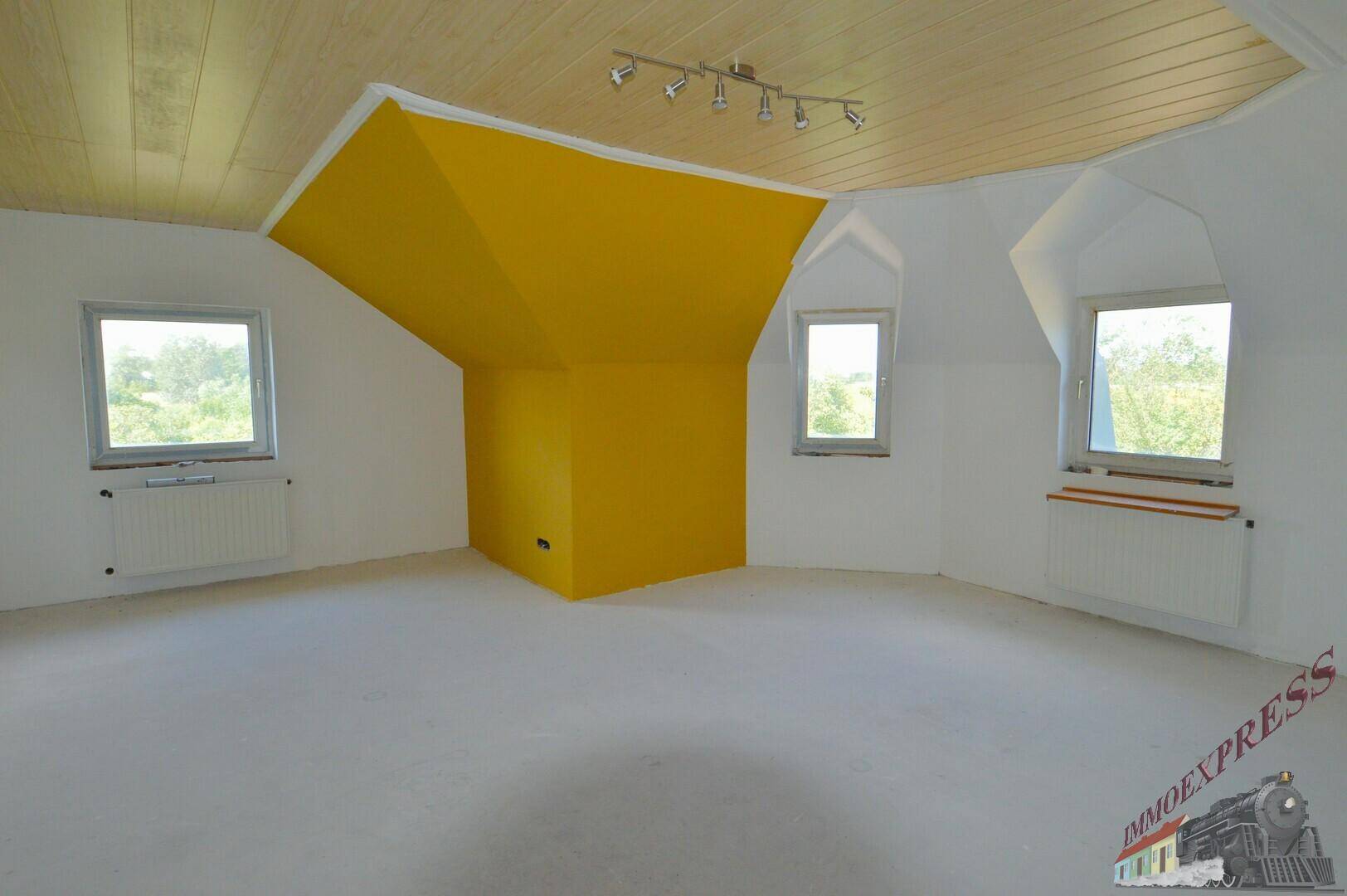 Geräumiges Dachgeschosszimmer mit gelber Akzentwand und mehreren Fenstern.