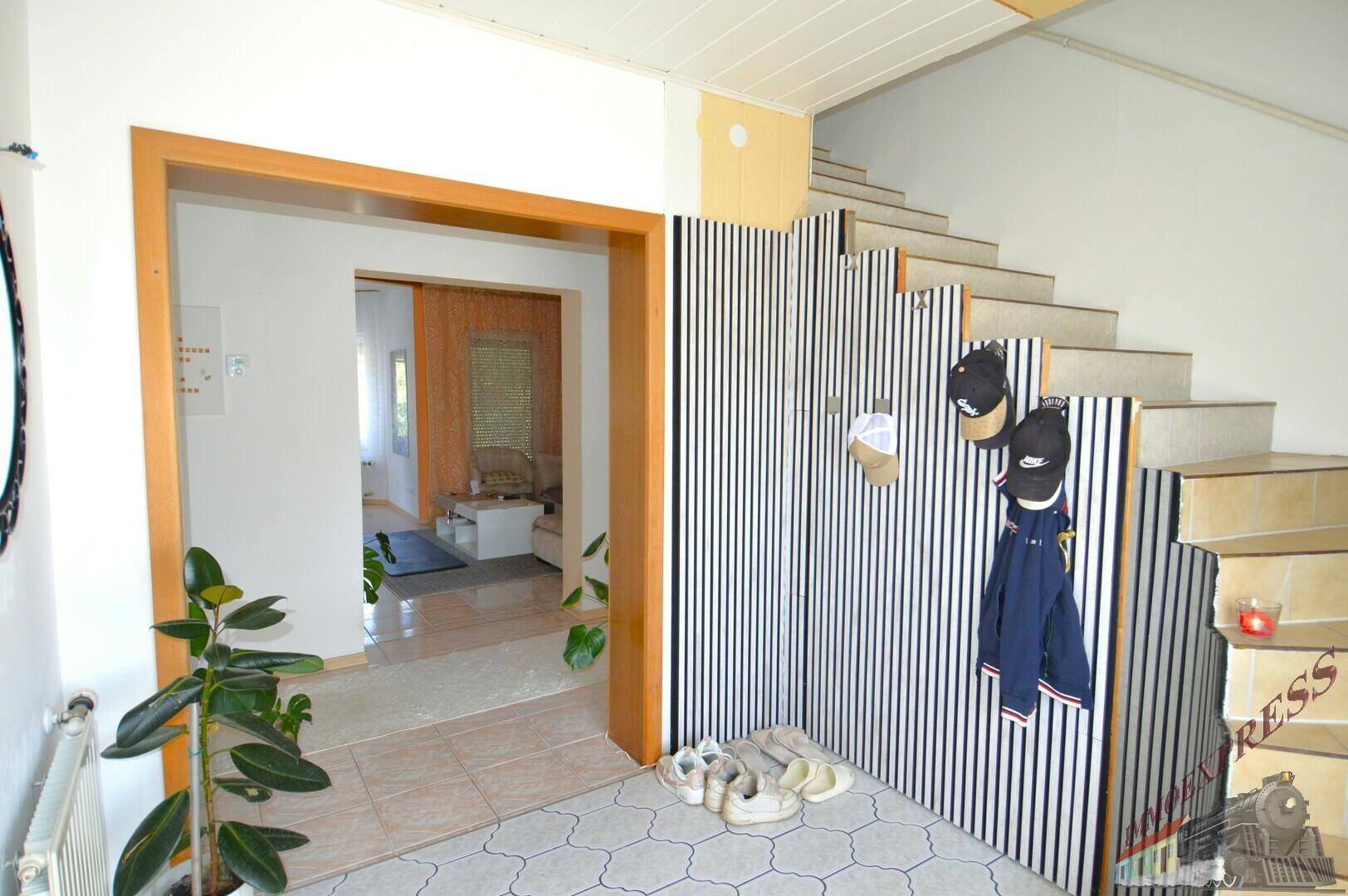 Heller Eingangsbereich mit gefliestem Boden, Garderobe und Treppenaufgang zum Obergeschoss.