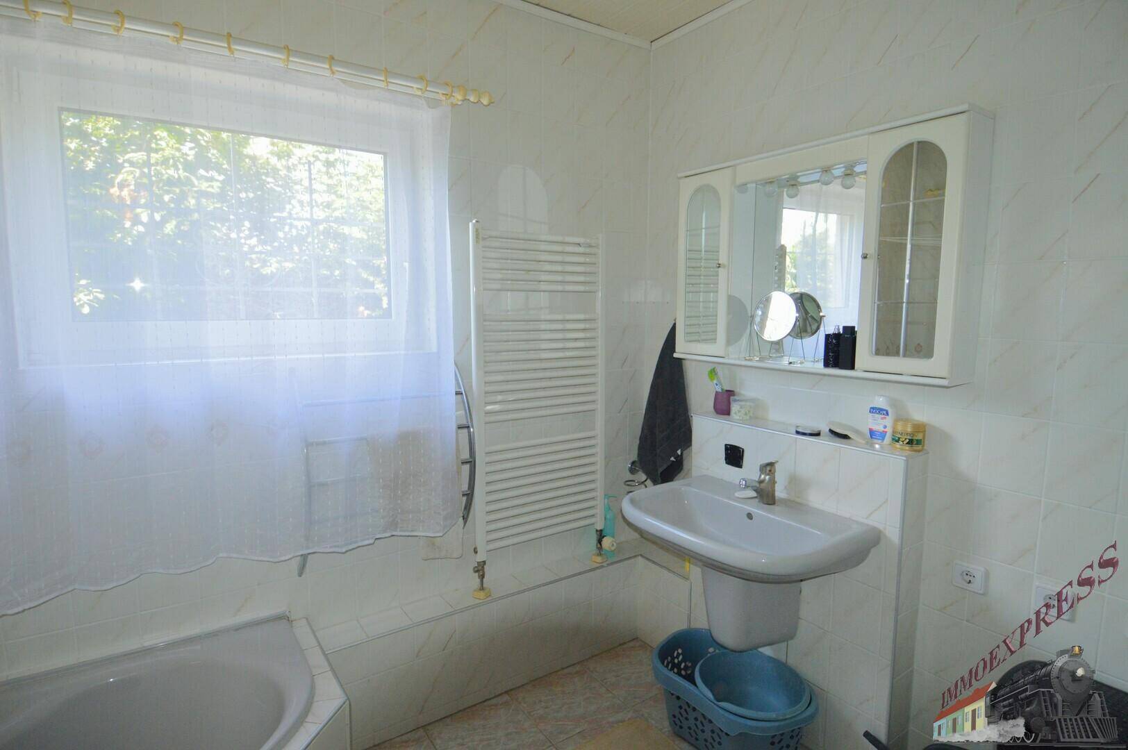 Badezimmer mit Waschbecken, Spiegelschrank, Handtuchheizkörper und Fenster.