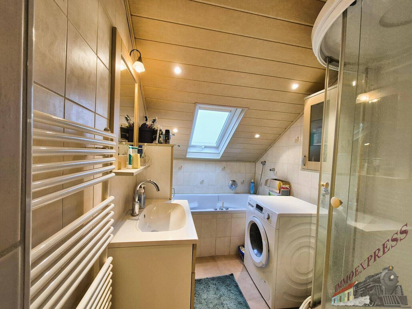 Badezimmer unter Dachschrägen mit Badewanne, Duschkabine, Waschbecken und Dachfenster.