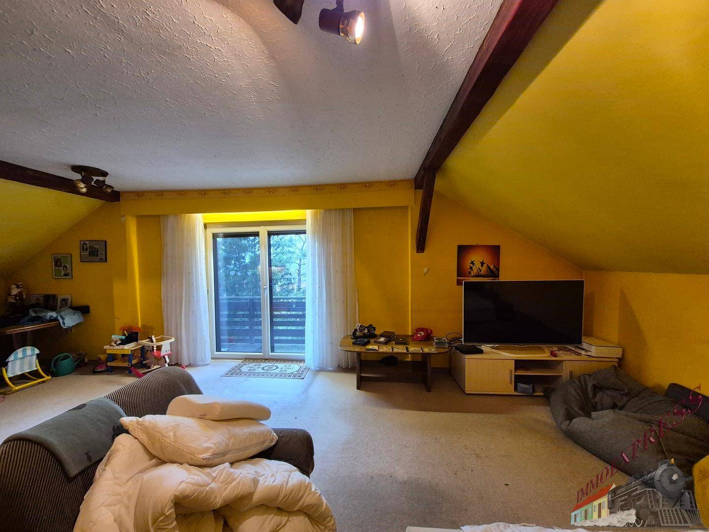 Helles Wohnzimmer mit gelben Wänden, Balkonzugang und Dachschrägen.