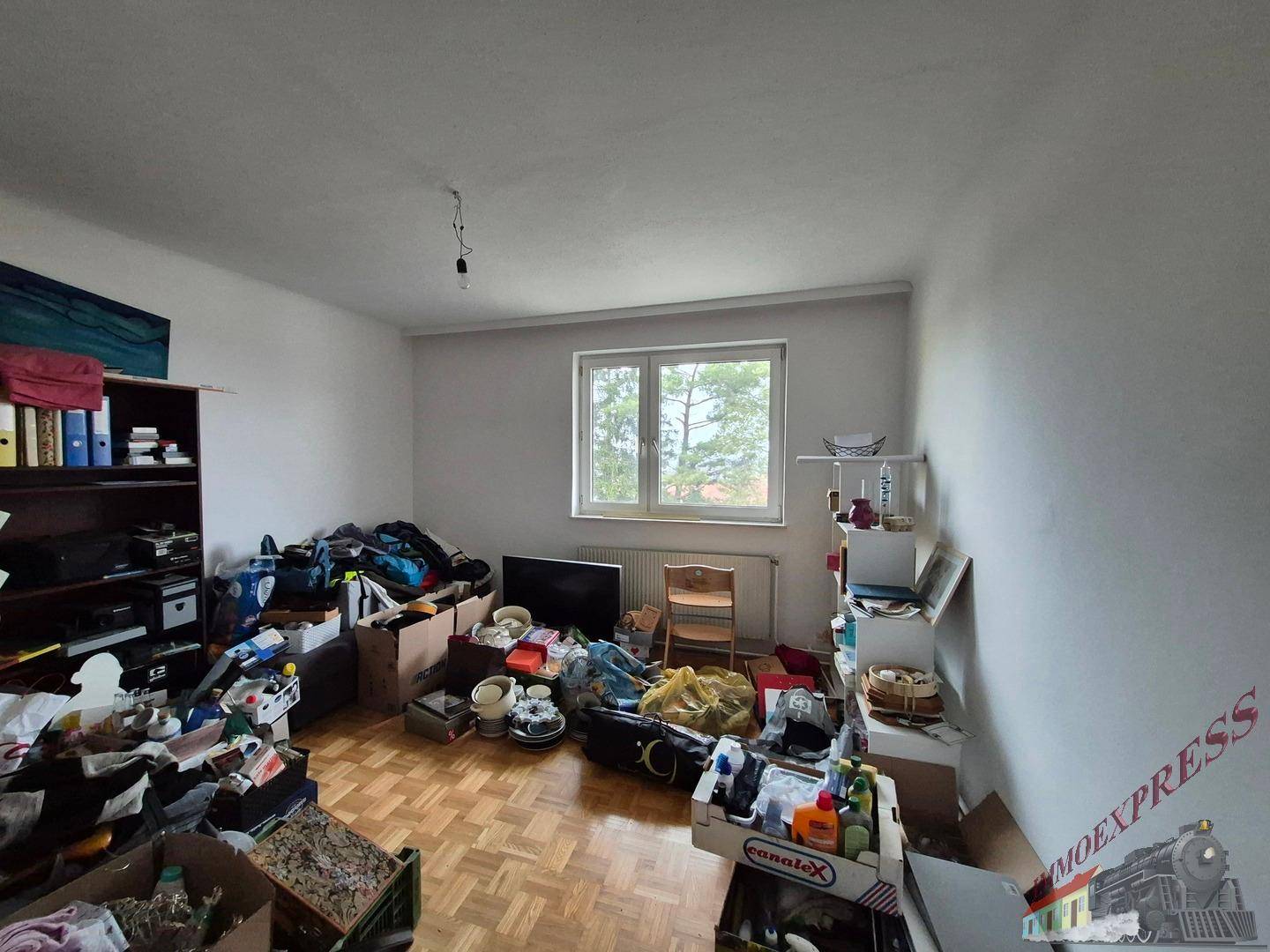 Unaufgeräumter Raum mit Parkettboden und einem Fenster, der als Lagerfläche dient.