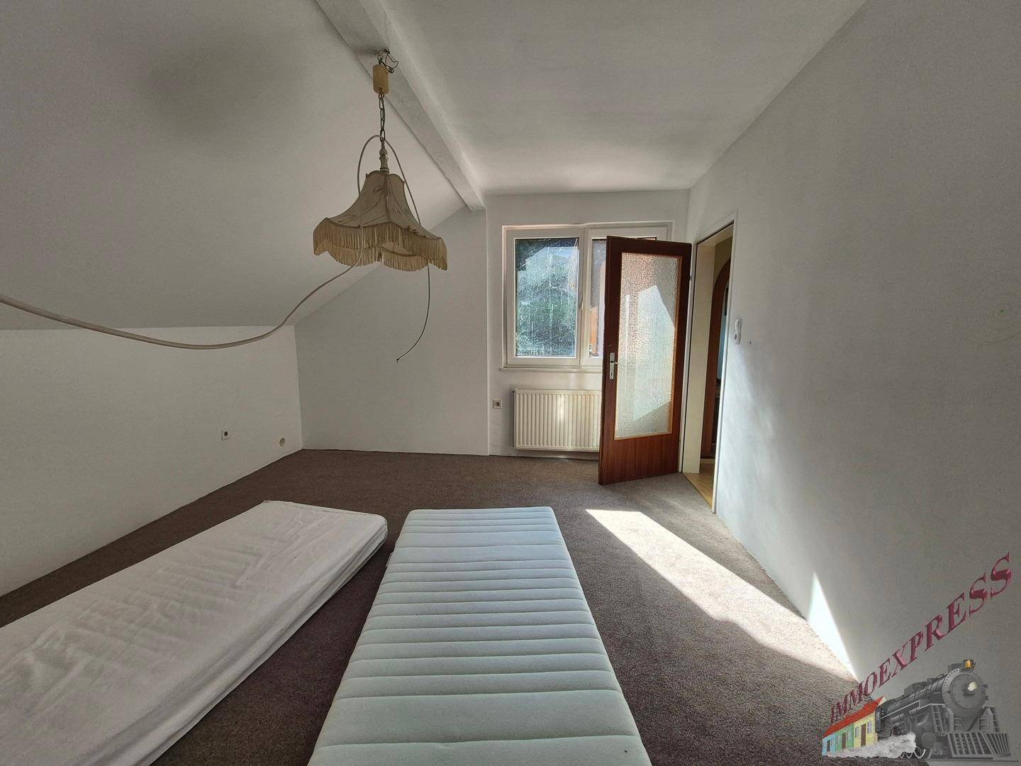 Leeres Schlafzimmer mit Teppichboden, einem Fenster und einfacher Beleuchtung.