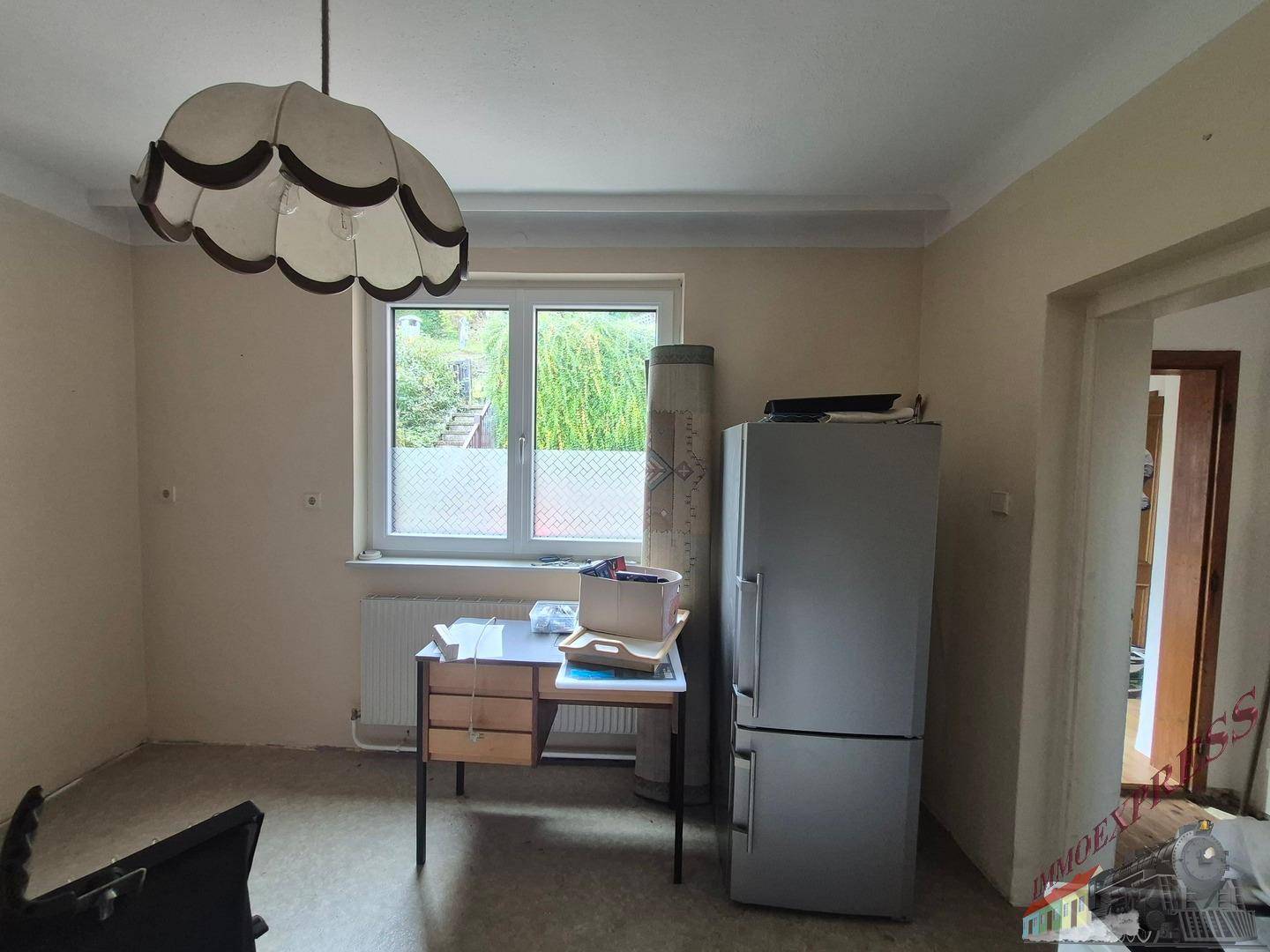 Raum mit Kühlschrank, Schreibtisch und Fenster, der als Abstellraum genutzt wird.