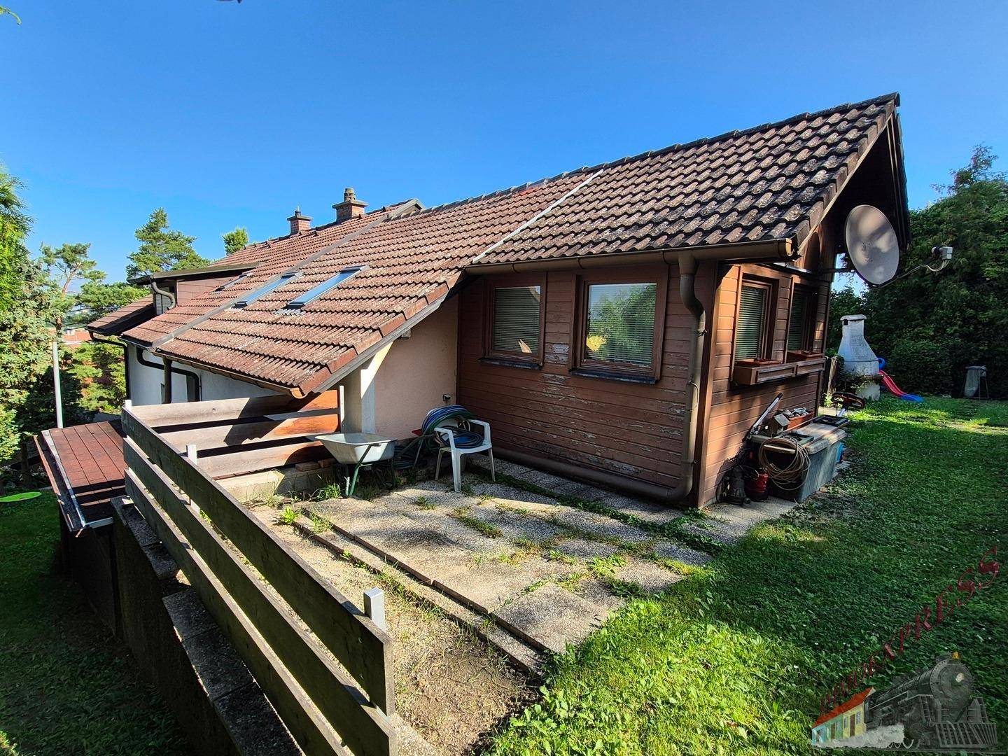 Seitlicher Gartenbereich des Hauses mit kleiner gepflasterter Fläche und üppigem Grün.