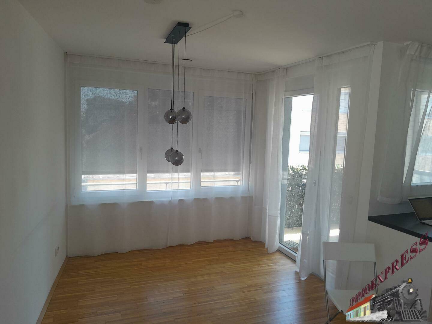 Heller Raum mit großen Fenstern, Parkettboden und Zugang zum Balkon.