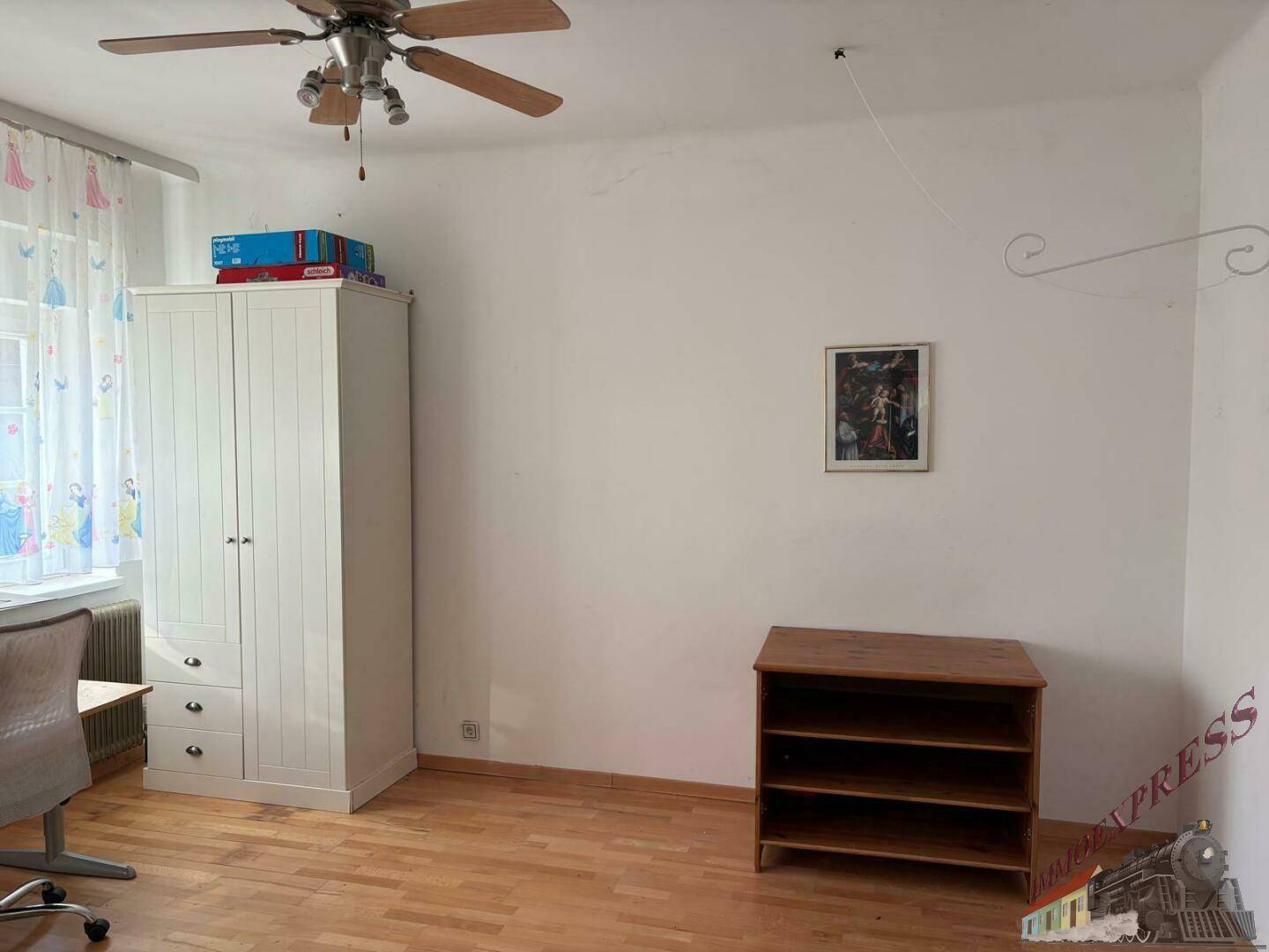 Schlaf- oder Kinderzimmer mit weißen Wänden, Holzfußboden, weißem Kleiderschrank und einem Fenster mit Vorhängen.