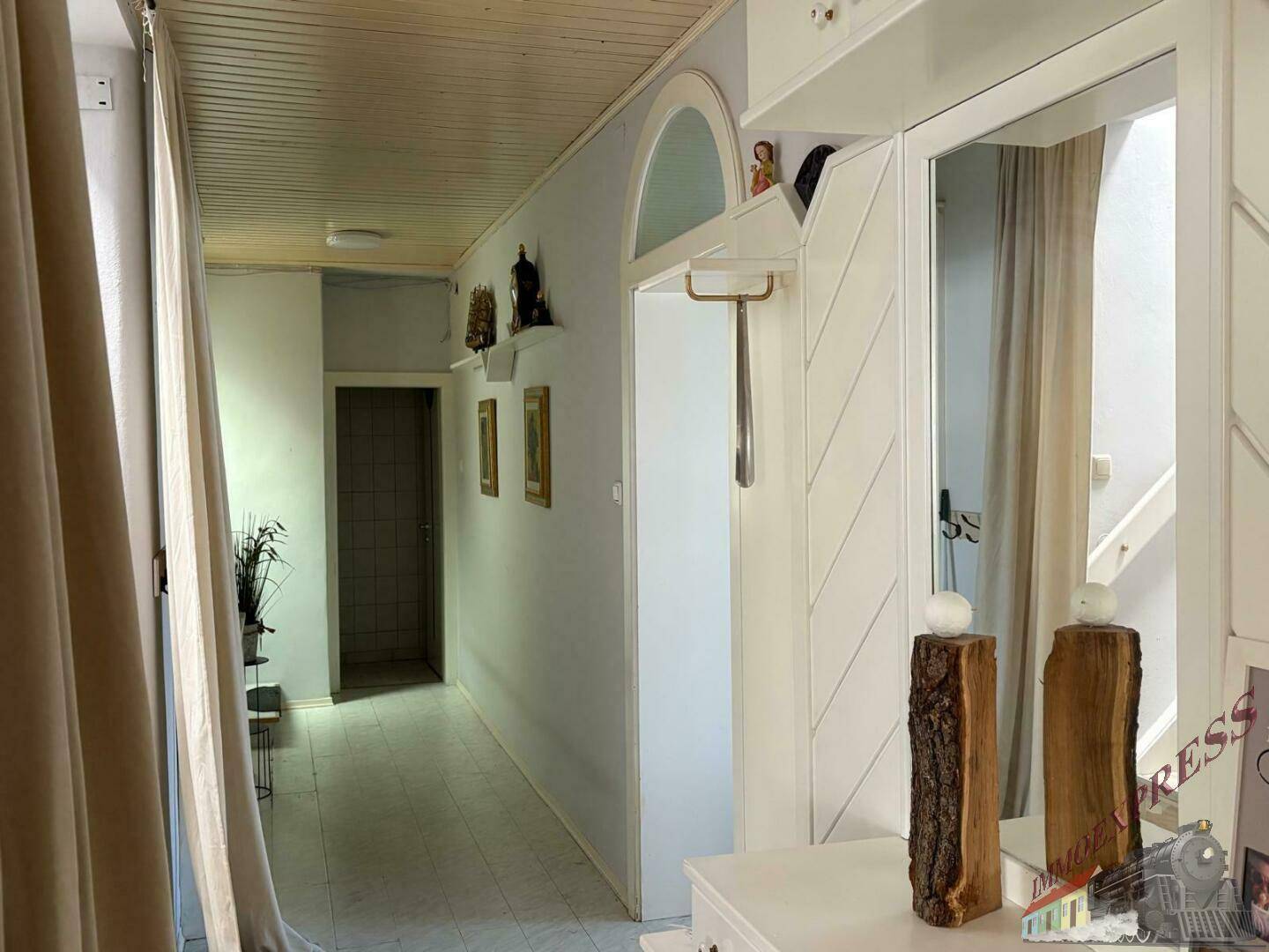 Heller Flur mit hellen Wänden, Fliesenboden und einer Holzpaneeldecke, ausgestattet mit Spiegel und Garderobe.