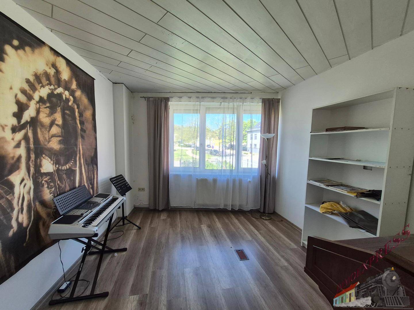 Wohnzimmer mit Holzboden, großer Fensterfront und einem Wandteppich als Dekoration.