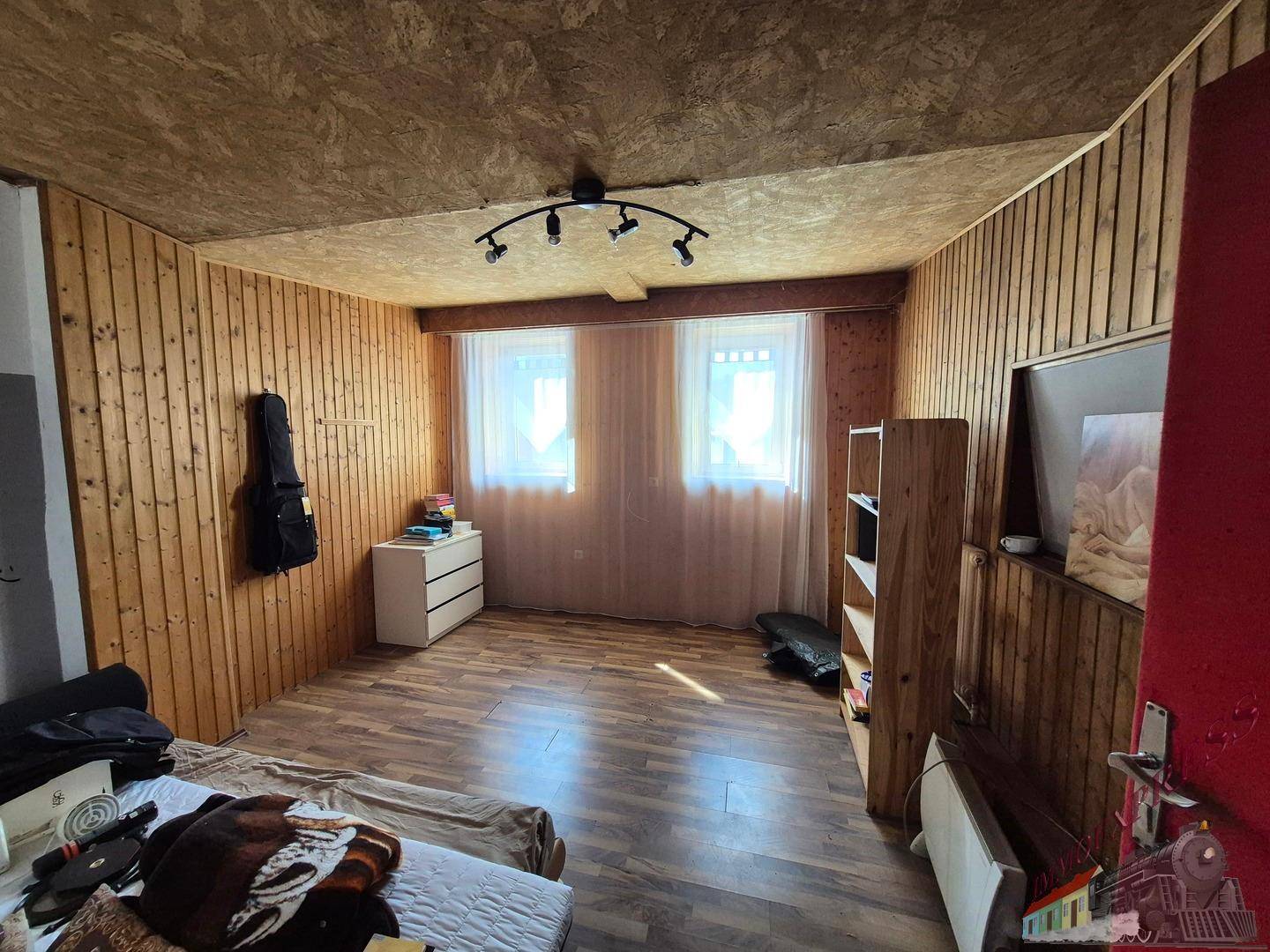 Schlafzimmer mit Holzvertäfelung, Laminatboden und zwei Fenstern für natürliches Licht.