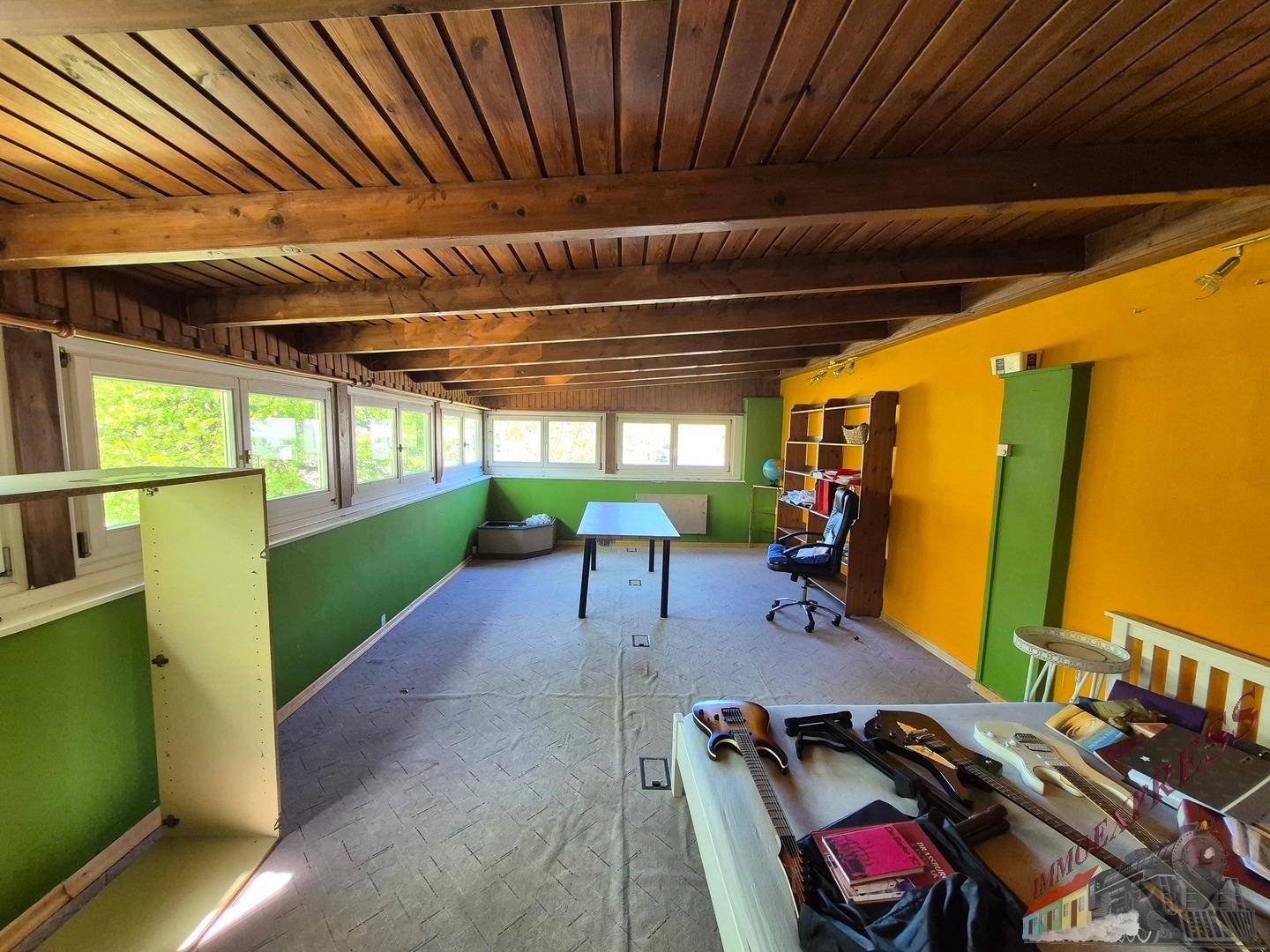 Kreativer Raum mit Holzbalkendecke, bunten Wänden und vielen Fenstern für Tageslicht.